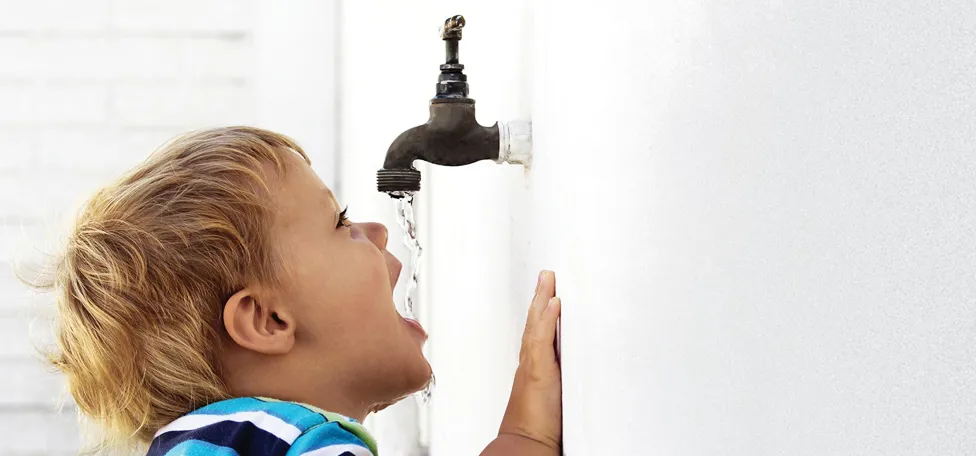 Lille dreng drikker af udendørs vandhane monteret i hvid væg