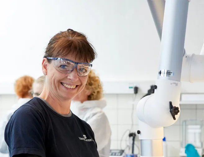 Smilende kvinde i laboratorium med handsker og beskyttelsesbriller