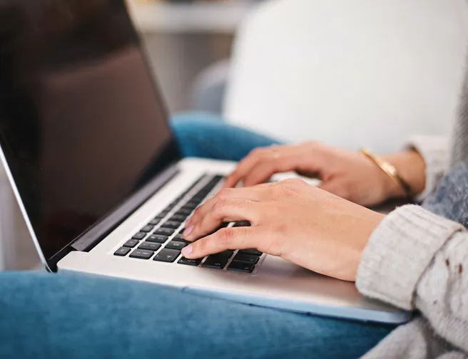 Nærbillede af person, der sidder med bærbar pc på skødet