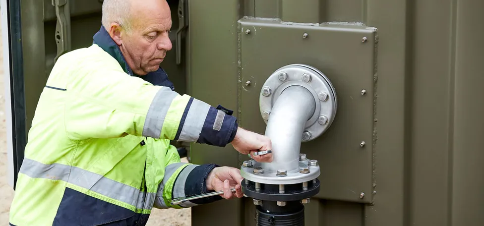 Mand i arbejdstøj skruer på rør ved vandboring