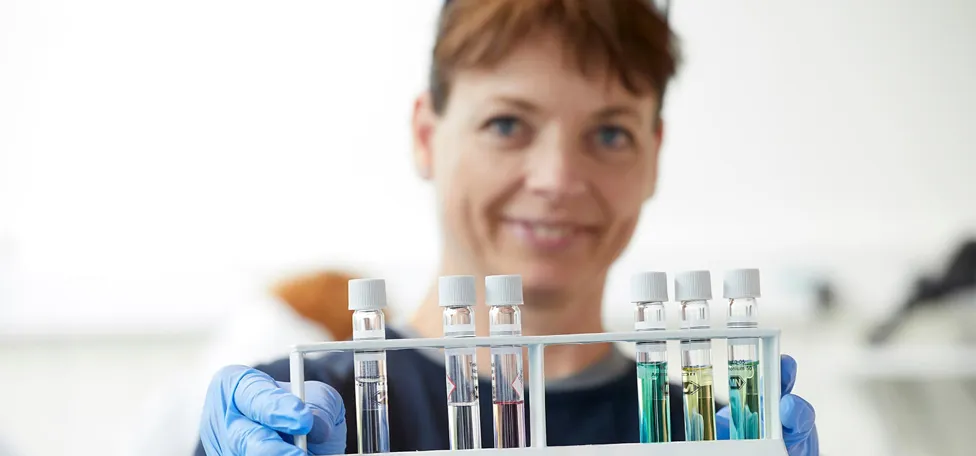 Kvinde iført blå plastichandsker holder et udvalg af små laboratorieglas frem