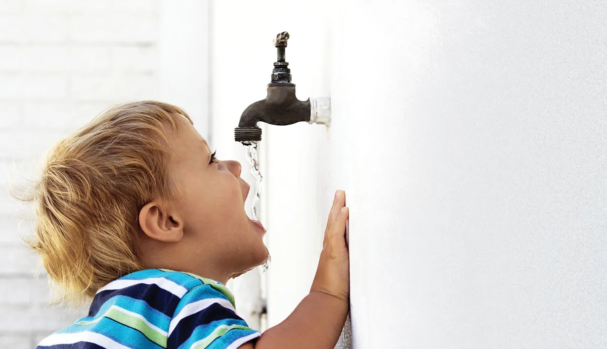 Dreng slukker tørsten under en udendørs vandhane.