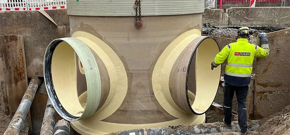 Mand i arbejdstøj arbejder ved stort kloakrør i byggegrube ved Odense Havn / Pakhuskajen