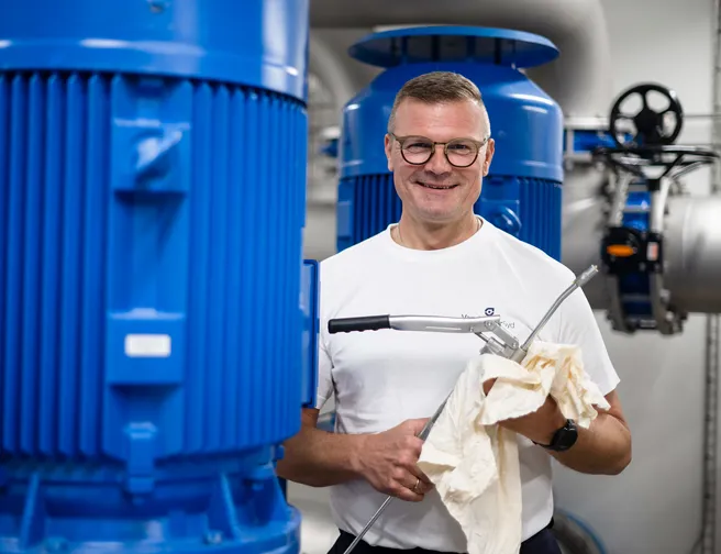 Smilende mand med værktøj omgivet af store blå pumper