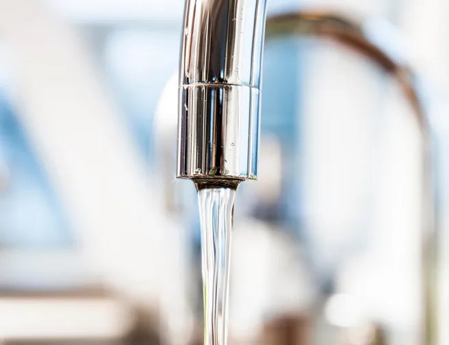 Nærbillede af vandstråle fra løbende vandhane, sløret baggrund