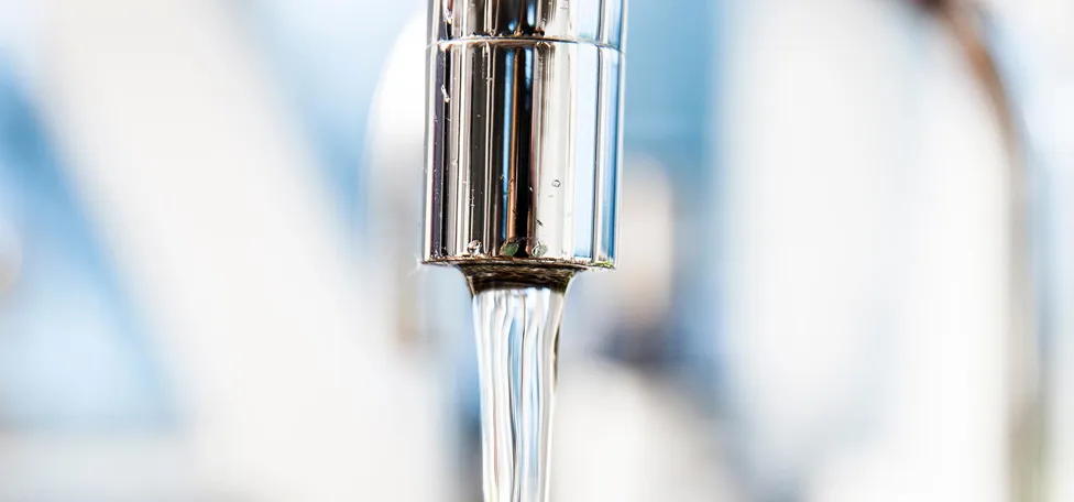 Nærbillede af vandstråle fra løbende vandhane, sløret baggrund