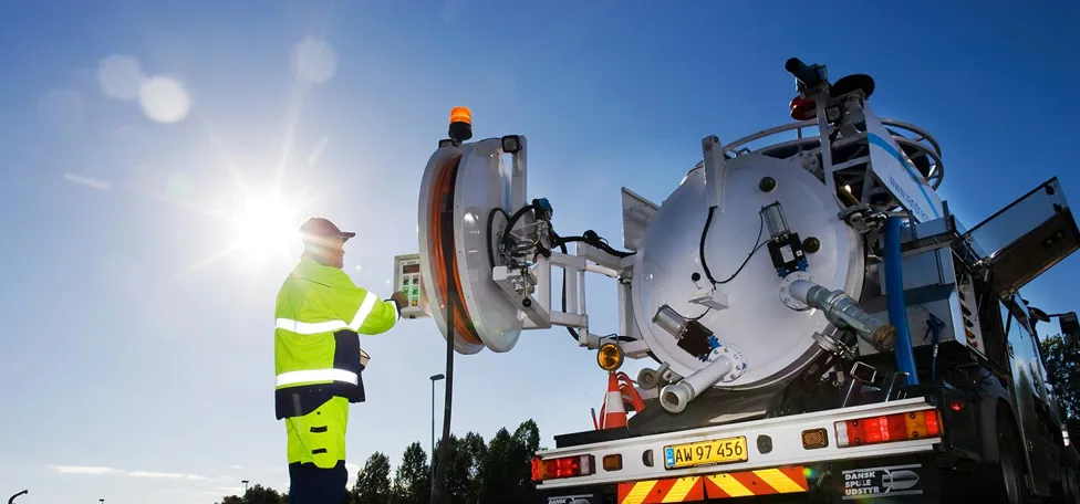 Mand i gult arbejdstøj står ved en spulebil / slamsuger