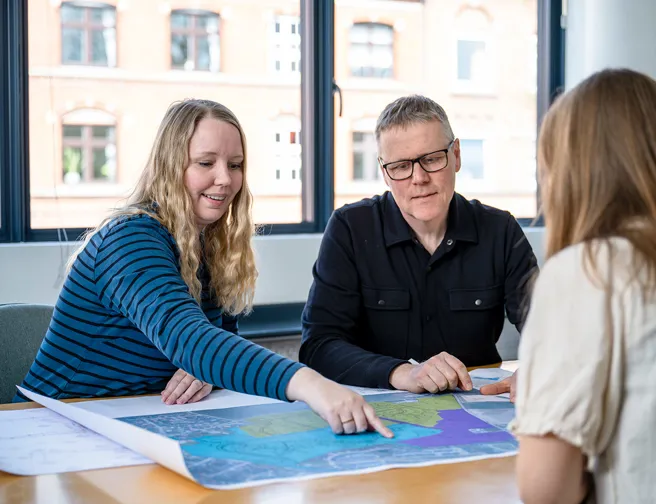 Tre mennesker omkring et mødebord, kigger på et kort i mange farver