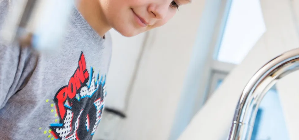 Dreng fylder kande med vand fra vandhane i lyst køkken