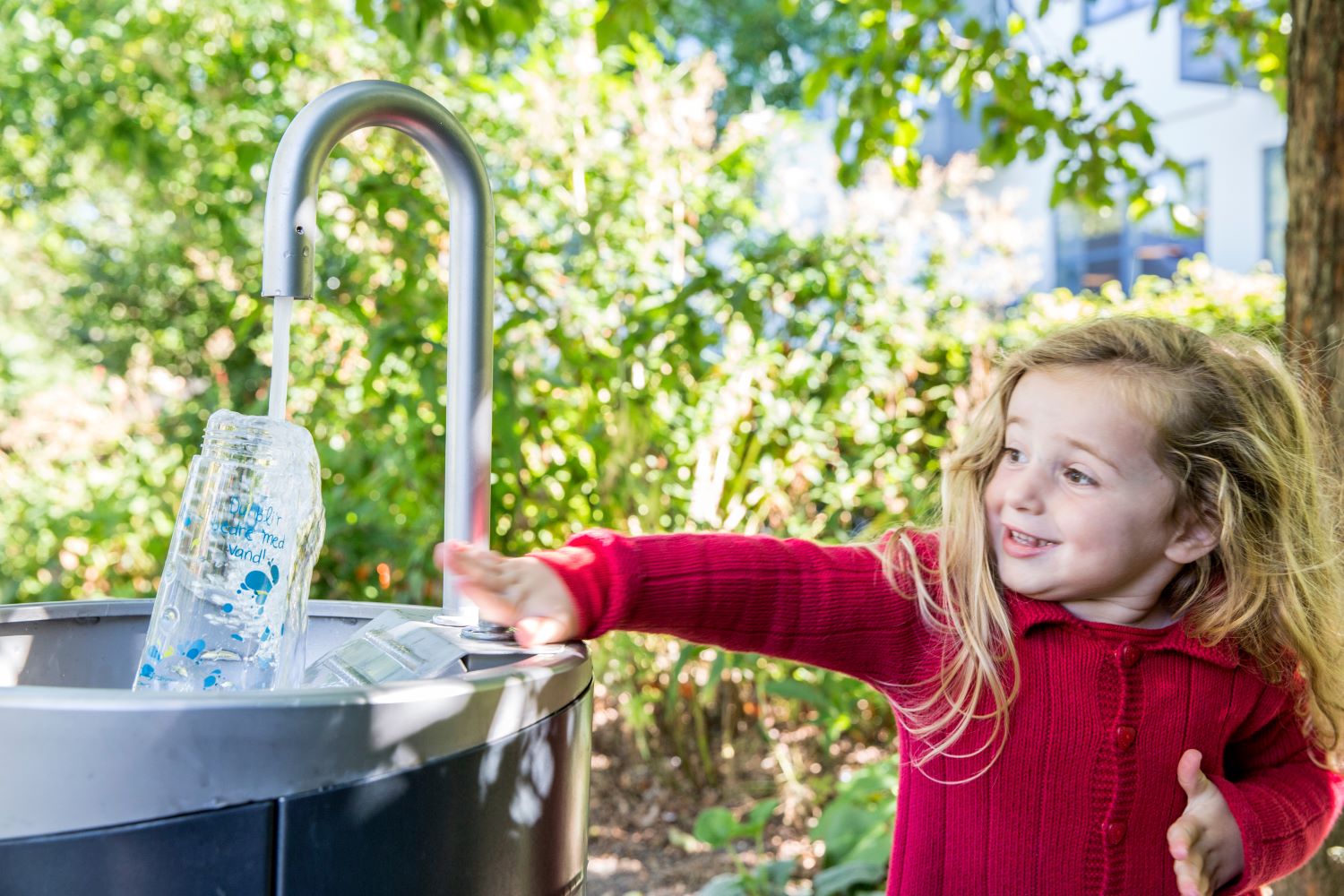 Pige ved vandpost ser på mens en drikkedunk fyldes.