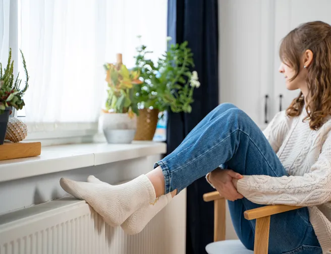 Ung kvinde sidder med fødderne på radiator
