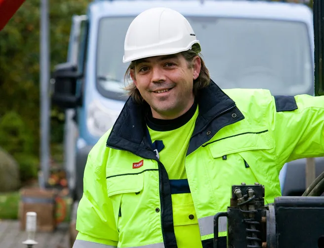 Smilende mand i gult arbejdstøj og sikkerhedshjelm kigger på kameraet