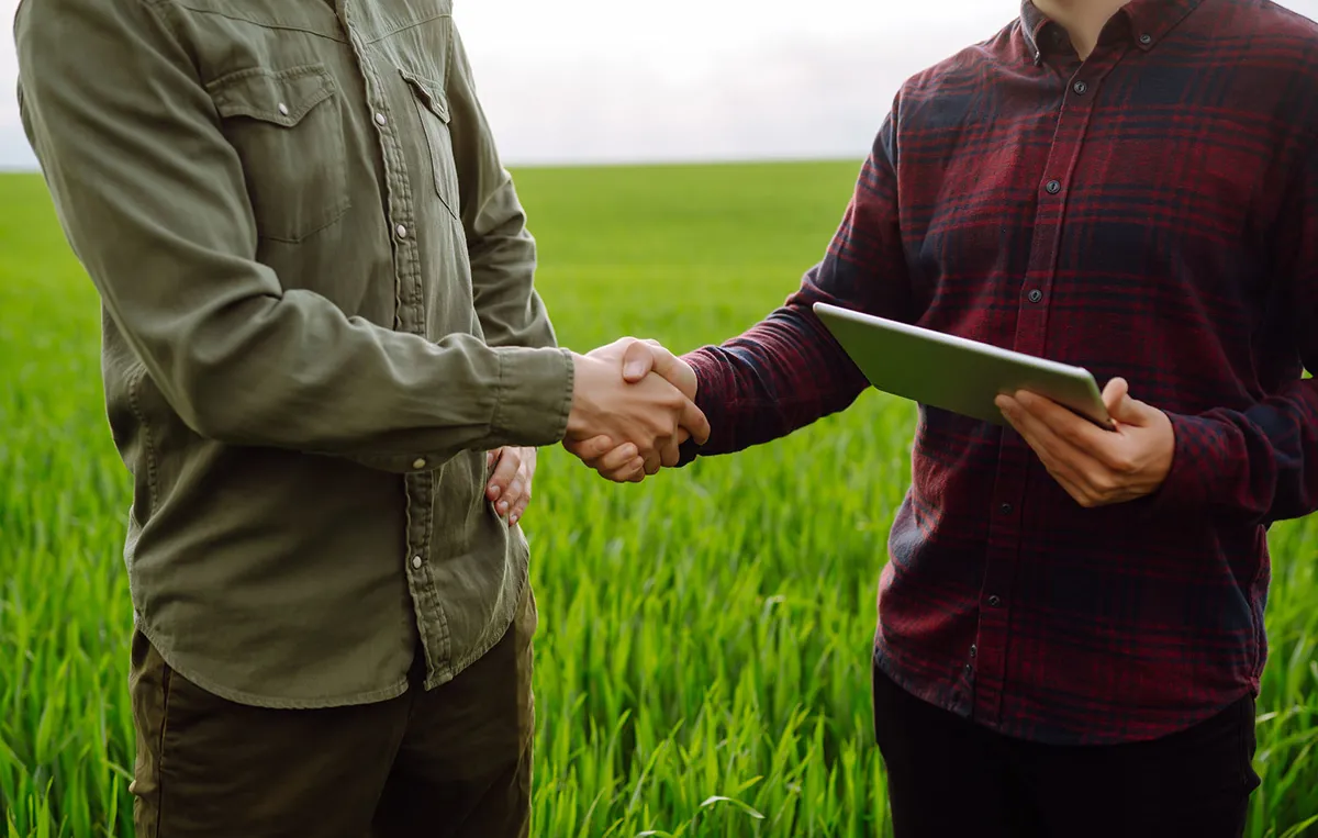 To personer giver hånden på en mark, som indikerer at en aftale er indgået.