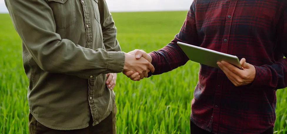 To personer giver hånden på en mark, som indikerer at en aftale er indgået.